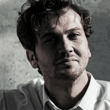 a man with a beard and a white shirt is looking at the camera
