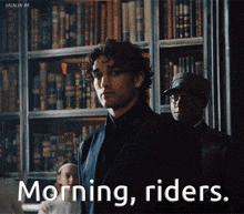 a man in a suit stands in front of a bookshelf with the words morning riders above him