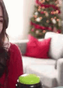 a woman in a red sweater is sitting on a couch holding a green button .