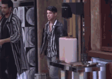 a man in a striped shirt is walking in front of a vending machine that says 00