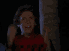 a man in a red shirt is making a funny face with his hands in the air .