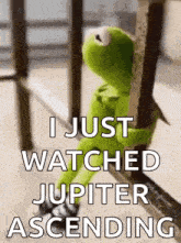 kermit the frog is sitting on a railing holding onto a railing and watching jupiter ascending .