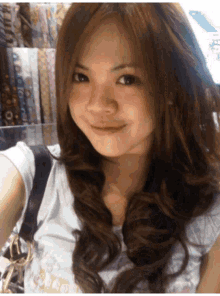 a woman with long brown hair is smiling and wearing a white shirt with a gucci logo on it