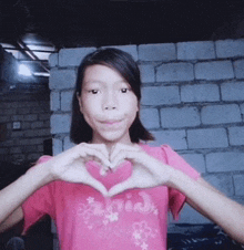 a girl in a pink shirt making a heart with her hands