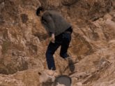 a man is walking down a rocky hillside with a dog behind him