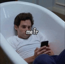 a man is sitting in a bathtub using a cell phone .