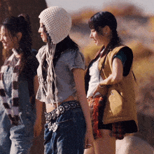 a woman wearing a knitted hat and overalls is standing next to two other women