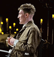 a man in a green jacket is sitting in a chair holding a cell phone and saying no .