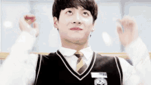 a young man in a school uniform and tie is making a heart shape with his hands .
