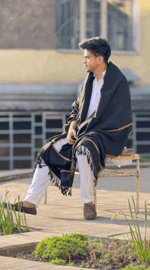 a man in a black blanket sits on a bench