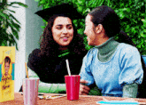 a woman in a graduation cap sits at a table with a friend
