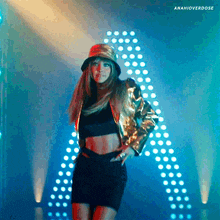 a woman wearing a bucket hat and a gold jacket stands in front of a large a