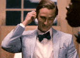 a man in a light blue suit and bow tie adjusts his ear