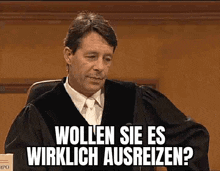 a man in a judge 's robe and tie is sitting in a courtroom and talking to someone .