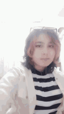 a girl with pink hair is wearing a striped shirt and glasses .