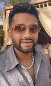the man is wearing sunglasses and a pearl necklace .