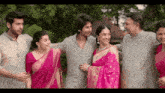 a group of people are posing for a picture and one of the women is wearing a pink saree