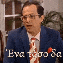 a man in a suit and tie is sitting at a table and talking in greek .