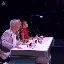 a group of people sit at a table with microphones and a star above them