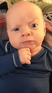 a baby in a blue shirt is making a funny face with his hand on his chin