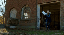 a woman in a blue suit is running in front of a brick building and throwing papers in the air