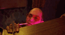 a bald man wearing sunglasses is smoking a cigarette in a dark room