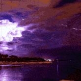 lightning strikes over a body of water with a purple sky