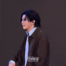 a man wearing a blue shirt and a brown jacket smiles