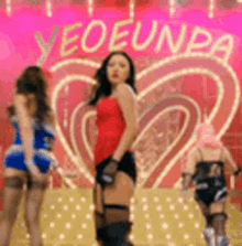 three women are dancing on a stage in front of a pink heart .