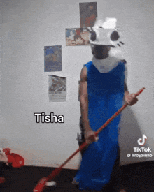 a man in a blue dress is holding a mop and the word tisha is on the wall behind him