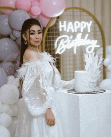 a woman in a white dress stands in front of balloons and a happy birthday sign