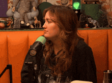 a woman is sitting in front of a microphone with a green button on the front