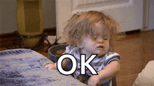 a little girl is sitting on a couch with the word ok written on her face .