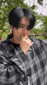 a young man with black hair is wearing a plaid shirt and holding his hand to his mouth .
