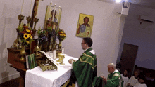 a priest in a green robe stands in front of an altar with flowers and candles