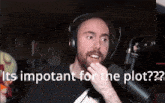a man wearing headphones stands in front of a microphone with the words " it 's important for the plot " behind him