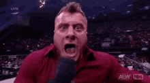 a man in a red shirt is holding a microphone in his mouth .
