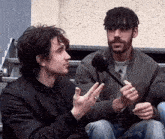 two men are sitting next to each other and one is holding a microphone in his hand