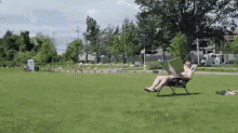 a man is sitting in a chair reading a book in the grass .