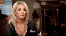 a woman in a black dress is standing in front of a fireplace and saying `` oops '' .