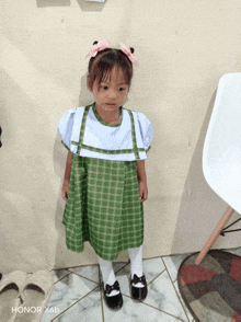 a little girl in a green and white dress is standing in front of a honor x6b