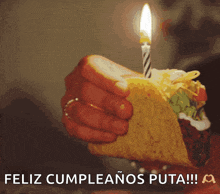 a person holding a taco with a lit candle and the words feliz cumpleanos puta written below