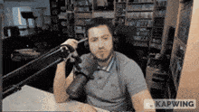 a man wearing headphones is sitting in front of a microphone with the word kapwing on the bottom