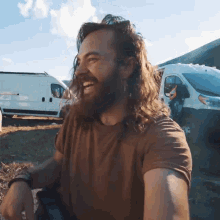 a man with long hair and a beard is standing in front of a white van