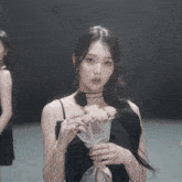 a girl in a black dress is holding a bouquet of flowers