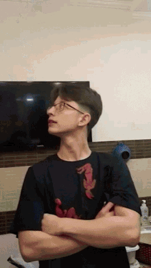a young man wearing glasses and a black shirt with a seahorse on it is standing with his arms crossed