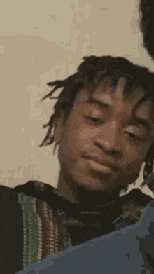 a young man with dreadlocks is making a funny face while looking at the camera .