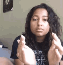 a young woman is sitting on a bed making a heart with her hands .