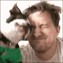 a man is making a funny face while a dog kisses him on the cheek .