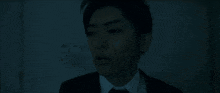 a man in a suit and tie is standing in the dark looking at the camera .